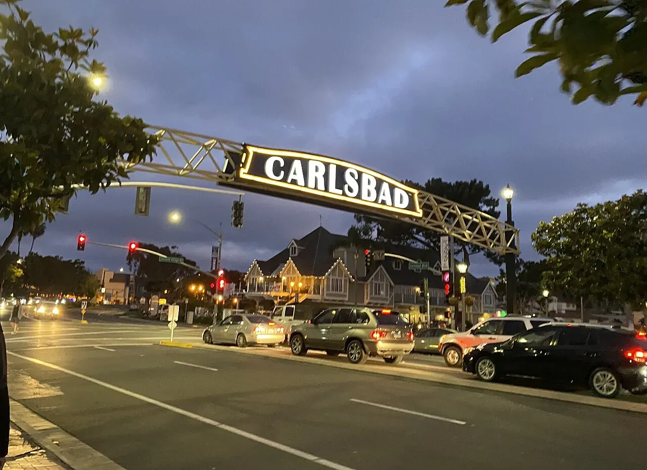 Carlsbad Village sign above Carlsbad Boulevard at dusk with cars and storefronts